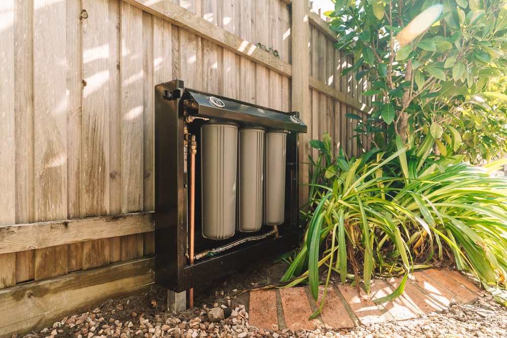 Whole-home water filter mounted against a side fence